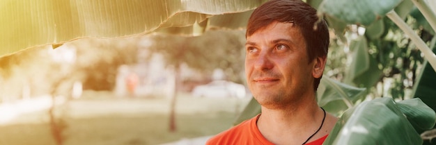 Retrato cara feliz sonriente sin afeitar maduro 40 años hombre viajero solo con rastrojo en el fondo de plantas verdes hojas de palma en la naturaleza en un día soleado de verano en vacaciones viajes escapada banner bengala