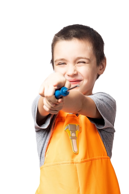 Retrato de un carpintero de niño sonriente con un mono de trabajo naranja, posando, sosteniendo un destornillador y apuntando a la cámara, divirtiéndose sobre un fondo blanco aislado. Disfraz infantil para unas vacaciones.