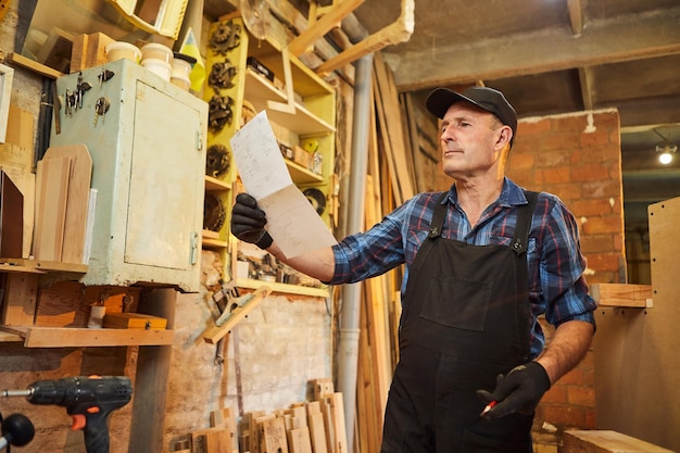 Retrato de un carpintero senior mirando planes de planos para hacer un mueble en el taller de carpintería