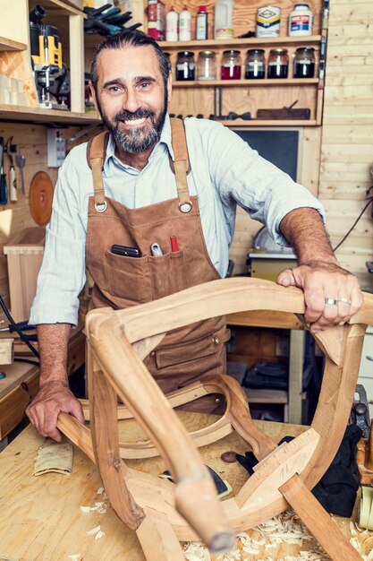 Foto retrato de un carpintero sonriente haciendo una silla en el taller