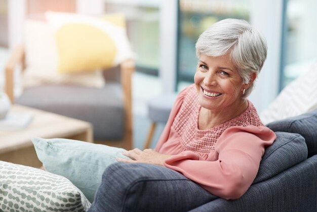 Retrato de casa y mujer mayor en el sofá relajarse y calmarse con la jubilación en la sala de estar Cara pensionista y anciana con descanso cómodo y descansando con paz felicidad y enfriamiento