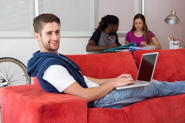 Retrato de casual joven usando la computadora portátil en el sofá