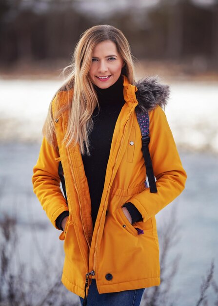 Retrato casual de una mujer joven en un cálido invierno amarillo anaranjado, con la cremallera bajada, sonriente, un paisaje nevado borroso detrás de ella