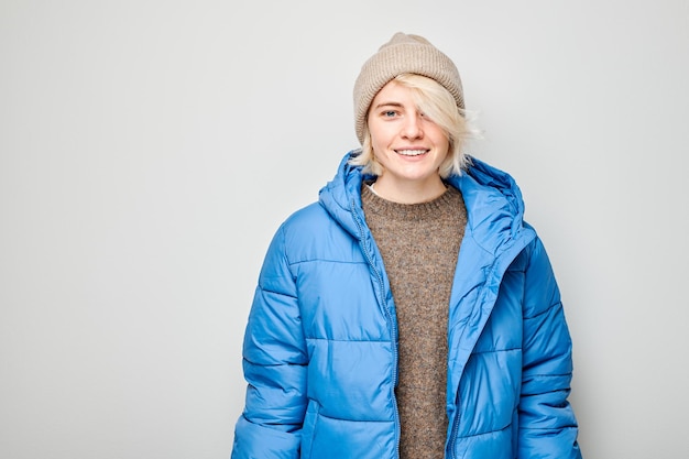 Retrato, caucásico, joven, mujer rubia, sonriente, alegremente, aislado, blanco, estudio, plano de fondo, feliz, niña, en, invierno, azul, chaqueta, y, sombrero, con, alegre, expresión facial