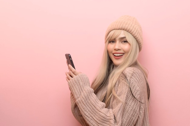 retrato, de, caucásico, mujer joven, llevando, suéter, tenencia, teléfono inteligente, encima, fondo rosa