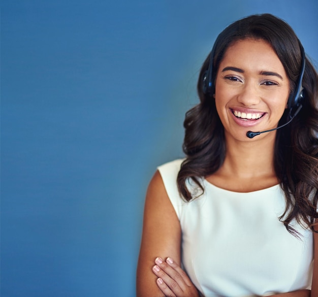 Retrato del centro de llamadas y mujer de negocios en el estudio con confianza telemarketing y servicio al cliente Mockup agente femenina y auriculares para escuchar audición y soporte para preguntas frecuentes por fondo azul