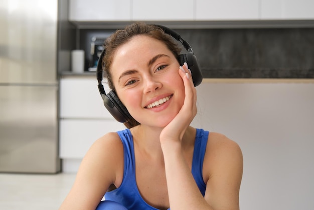 Un retrato de cerca de una hermosa chica morena con ropa deportiva se sienta en auriculares inalámbricos y escucha