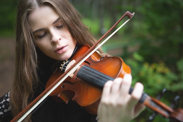Retrato de cerca de una hermosa niña violinista que bajó los ojos con entusiasmo tocando el violín obra romántica