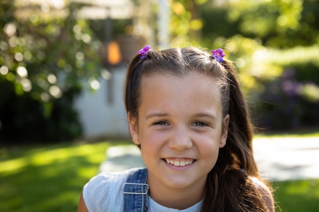 Retrato de cerca de una joven caucásica con cabello castaño largo y ojos azules afuera en un jardín soleado sonriendo a la cámara. Familia disfrutando del tiempo en casa, concepto de estilo de vida