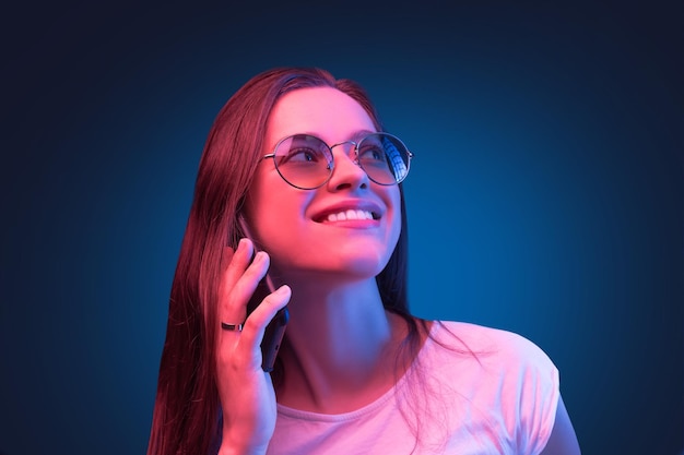 Retrato de cerca de neón de una joven con gafas de sol redondas hablando con un teléfono inteligente