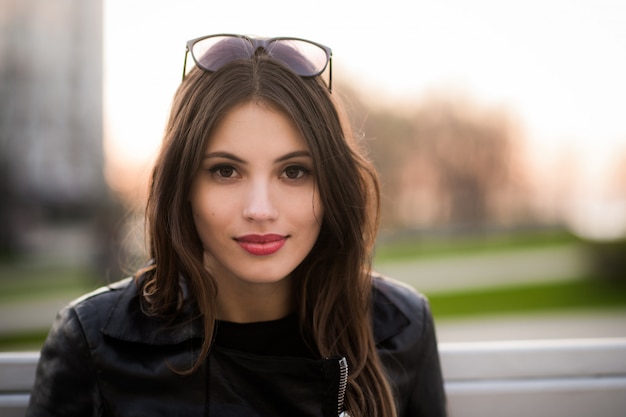 Retrato cercano de la bella joven morena sonriente, contra el parque verde del verano en la puesta del sol