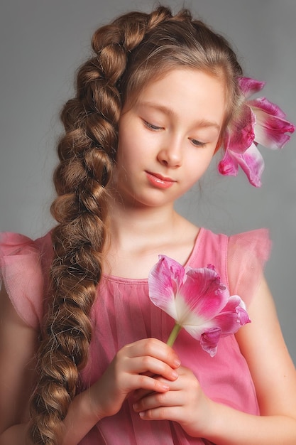 Retrato cercano de una chica con el pelo largo con una flor de orquídea en un fondo gris