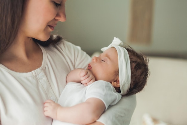 Retrato cercano de una linda niña recién nacida de cabello oscuro con un traje blanco en los brazos de una joven madre Maternidad Padre Sueño saludable