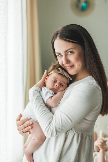 Foto retrato cercano de una linda niña recién nacida de cabello oscuro con un traje blanco en los brazos de una joven madre maternidad padre sueño saludable