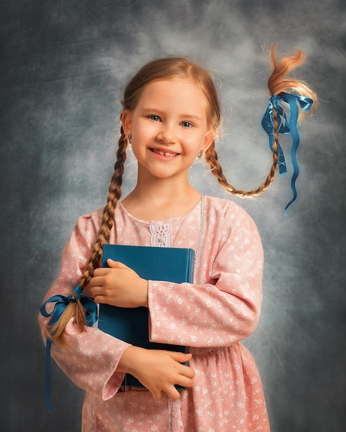 Retrato cercano de una niña feliz con dos trenzas voladoras sobre un fondo gris con libro