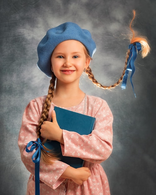 Retrato cercano de una niña feliz con dos trenzas voladoras sobre un fondo gris con libro