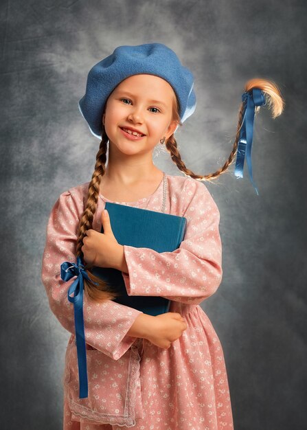 Retrato cercano de una niña feliz con dos trenzas voladoras sobre un fondo gris con libro