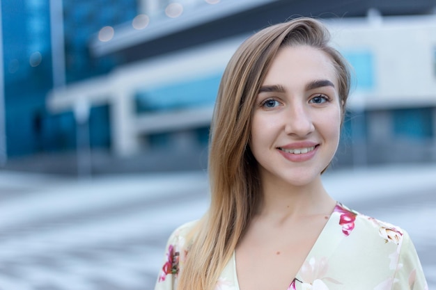 Retrato cerrado de una hermosa joven sobre un fondo de un centro de negocios azul vestido con un vestido beige de verano