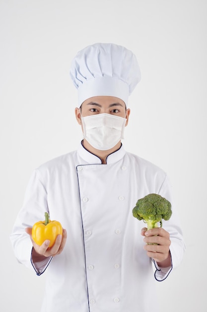 Retrato de chef de café con sombrero y máscara protectora con pimiento y brócoli
