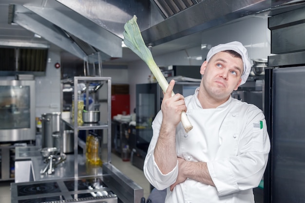 Retrato del chef en la cocina del restaurante pensando y sosteniendo un puerro