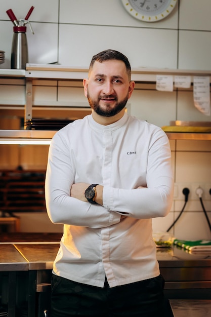 Retrato de chef jefe masculino caucásico barbudo en uniforme blanco en la cocina del restaurante