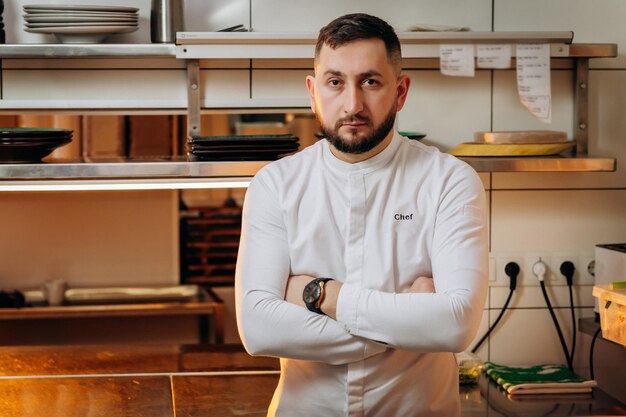 Retrato de chef jefe masculino caucásico barbudo en uniforme blanco en la cocina del restaurante