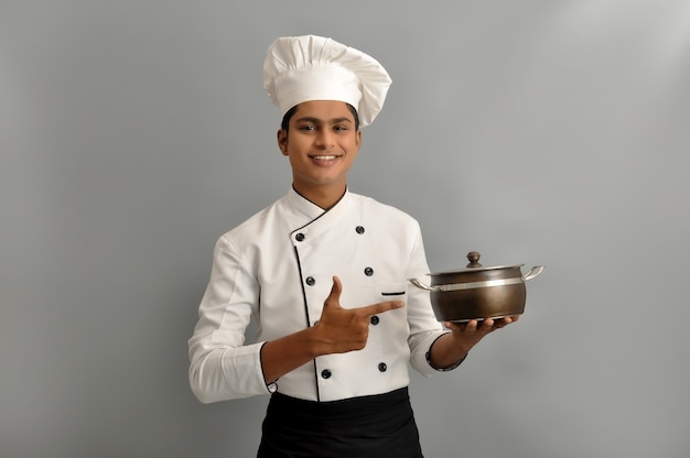 Retrato de un chef masculino feliz vestido con uniforme sosteniendo la olla y apuntando