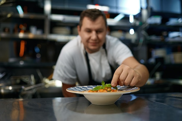 Retrato de un chef satisfecho colocando hojas de albahaca en un plato con pasta recién cocinada, enfoque selectivo. Comida tradicional, concepto de alimentación saludable.