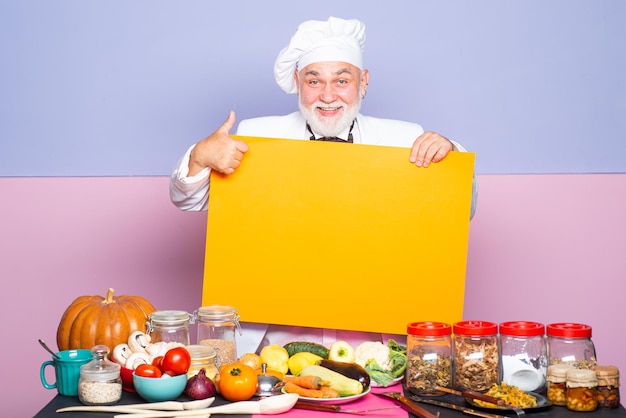 Foto retrato de un chef sonriente señalando en un tablero chef senior señalando con el dedo en el menú del tablero en blanco