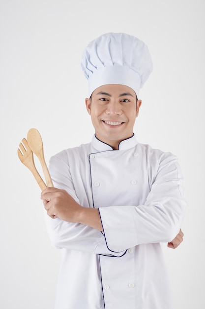 Retrato de chef sonriente con sombrero y uniforme sosteniendo espátulas de madera