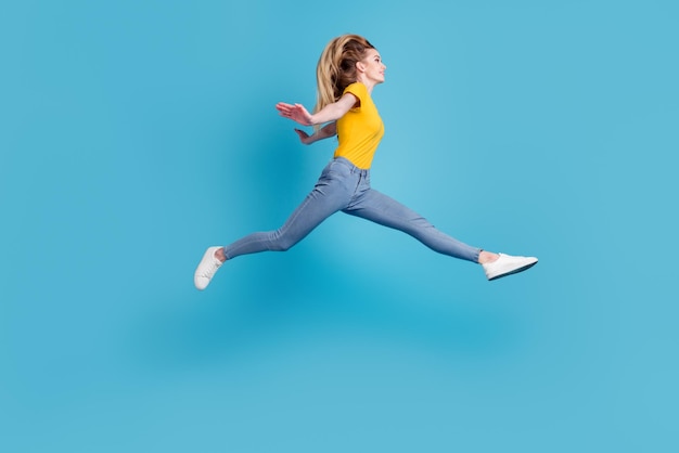 Retrato de una chica activa deportiva en movimiento saltando en el aire aislada en un fondo azul con un estiramiento perfecto