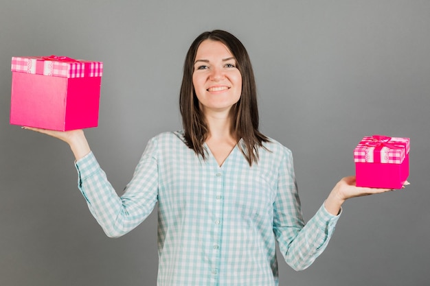 Retrato de una chica alegre y hermosa con una sonrisa brillante sosteniendo dos regalos en sus manos mirando a la cámara aislada en un concepto de publicidad de fondo gris