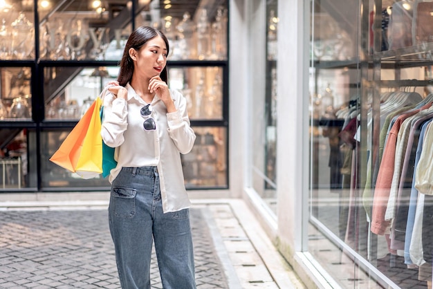 Retrato de una chica asiática emocionada hermosa chica feliz sonriendo con bolsas de compras expresión relajada Emociones positivas concepto de estilo de vida de compras