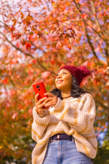 Retrato de una chica asiática en otoño con un móvil sonriendo en un bosque de concepto de tecnología de hojas rojas