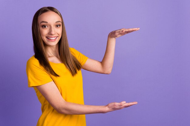 Retrato de una chica atractiva y alegre que muestra el espacio de copia del producto aislado de fondo de color púrpura violeta