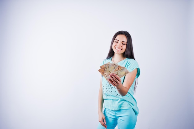 Retrato de una chica atractiva con camiseta azul o turquesa y pantalones posando con mucho dinero en la mano