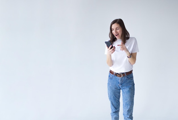 Retrato de una chica atractiva increíble sosteniendo un teléfono móvil y mirando a la cámara aislada