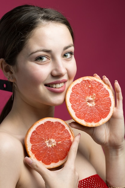 Retrato de una chica atractiva que sostiene una rodaja de pomelo en rodajas sobre un fondo rojo.