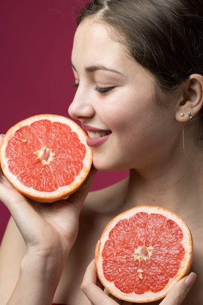 Retrato de una chica atractiva que sostiene una rodaja de pomelo en rodajas sobre un fondo rojo.