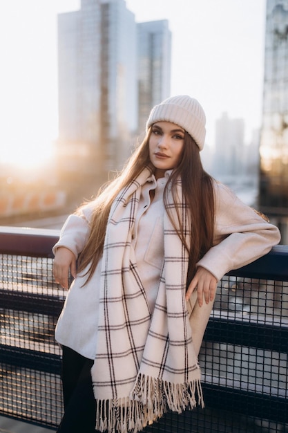 Retrato de una chica bonita en el fondo de la ciudad Vista frontal de una chica hermosa vestida con sombrero blanco y bufanda a cuadros