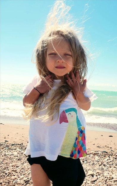 Retrato de una chica con el cabello desordenado de pie en la playa
