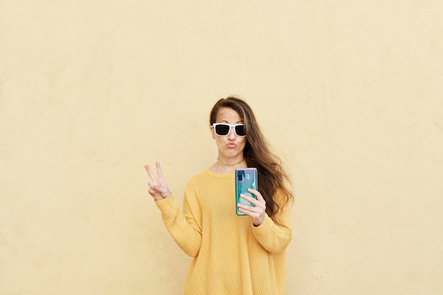 Retrato chica cool con gafas de sol enviando beso de aire dulce sosteniendo el teléfono