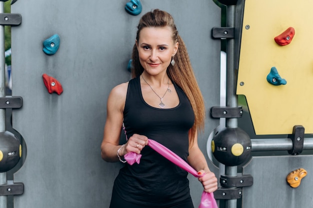 Retrato de una chica delgada de fitness se pone de pie y estira la banda elástica con las manos contra el