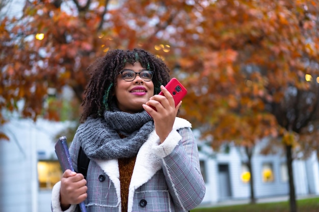 Retrato de una chica étnica negra caminando en la universidad en otoño hablando por teléfono de regreso a la escuela