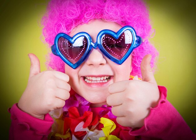 Foto retrato de una chica feliz con una peluca rosa mostrando los pulgares hacia arriba contra un fondo amarillo