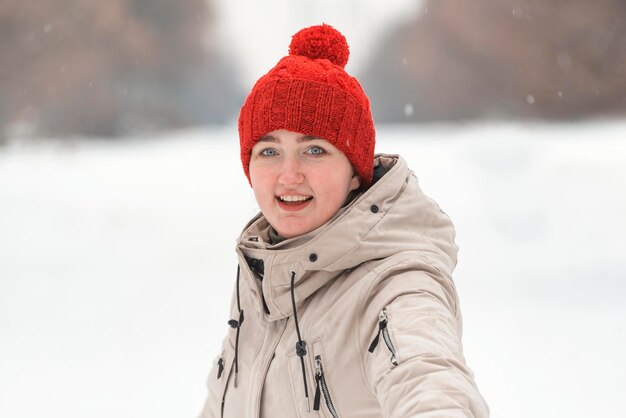 Foto retrato de chica feliz con sombrero de punto rojo con bubo en el fondo del parque de nieve mujer con ropa de invierno afuera