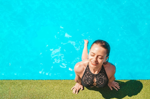 Retrato de chica en forma de moda en traje de baño con ojos cerrados disfrutando de la luz del sol de descanso sobre fondo de agua azul, concepto de viaje de viaje de viaje de turismo de viaje. espacio vacío para prueba y diseño.