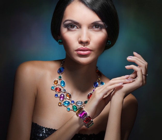 Foto retrato de una chica glamorosa con cabello negro y un collar caro con piedras preciosas y de colores