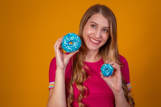 Retrato de una chica guapa alegre sosteniendo donas azules en su cara