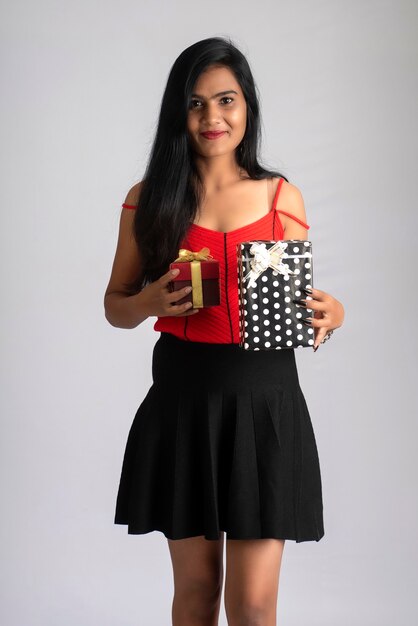 Retrato de una chica guapa sosteniendo y posando con caja de regalo sobre fondo gris